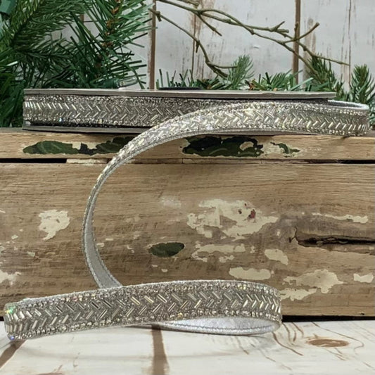 A silver bead chevron embellishment placed on a wooden surface with a blurred pine tree in the background.
