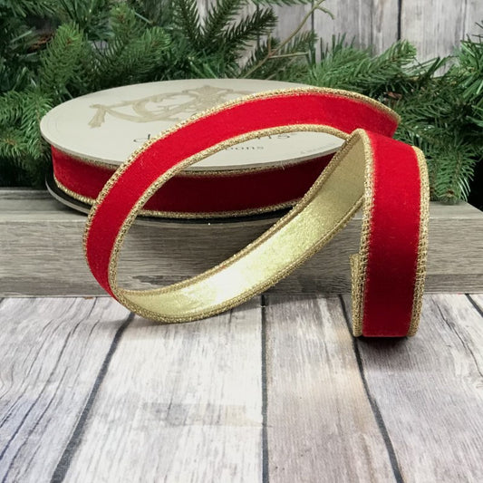 A 1-inch wide red velvet ribbon with gold glitter trim, displayed on a wooden surface with a blurred greenery background.