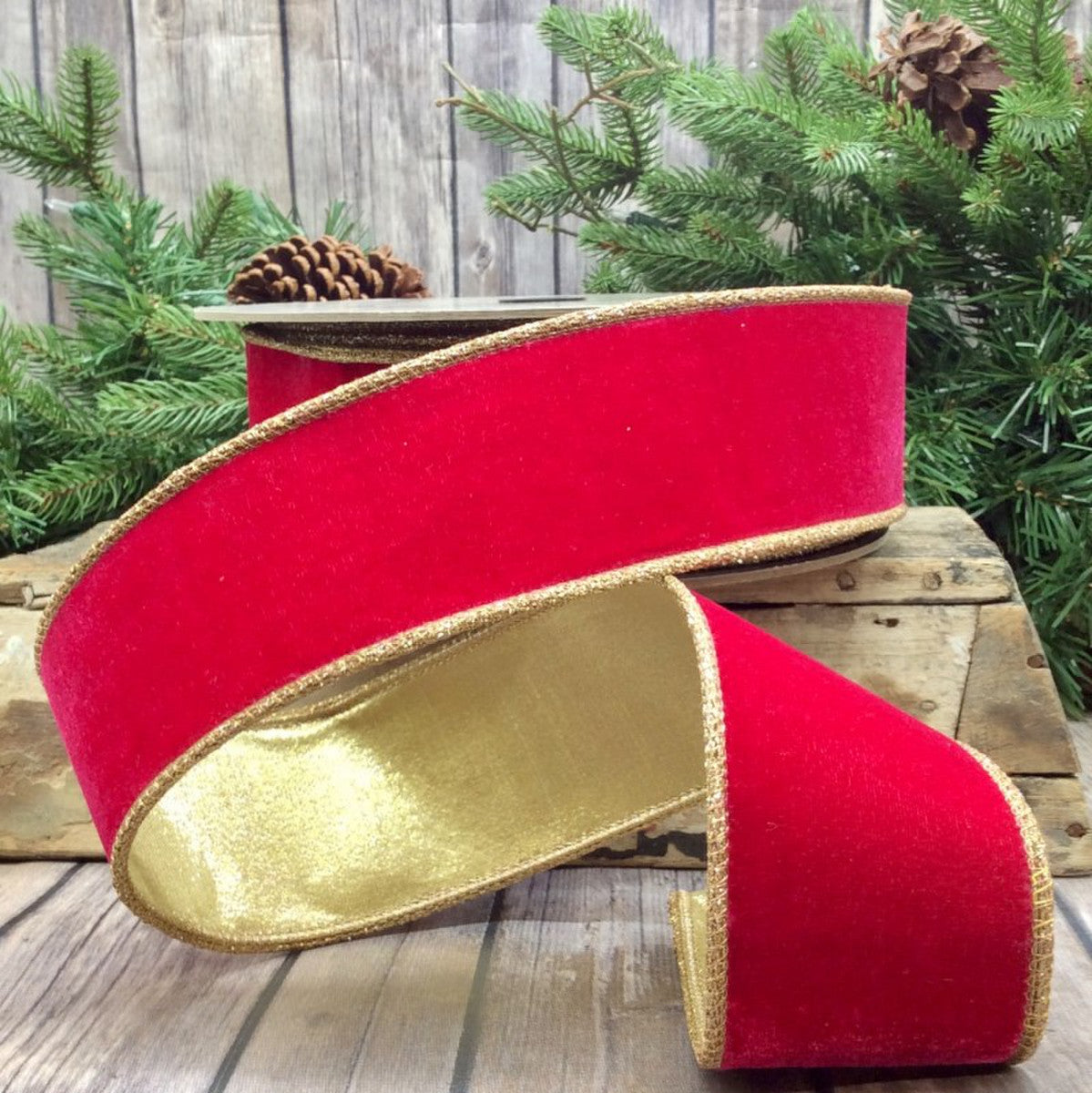 A 2.5-inch wide red velvet ribbon with gold glitter trim, displayed on a wooden surface with a blurred greenery background.