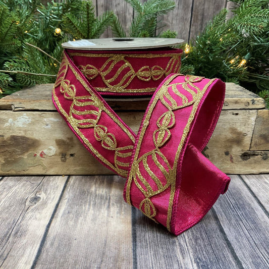 A 2-inch wide metallic dupion gold bullion ornament ribbon with intricate gold detailing, displayed on a wooden surface with Christmas lights in the background.