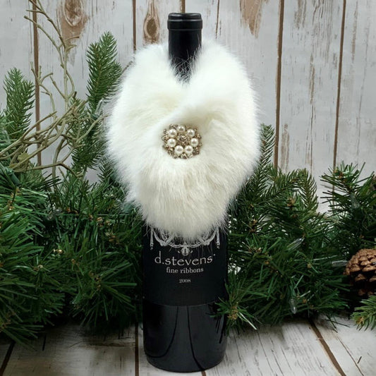 Decorative wine bottle with white fur and brooch against a wooden background