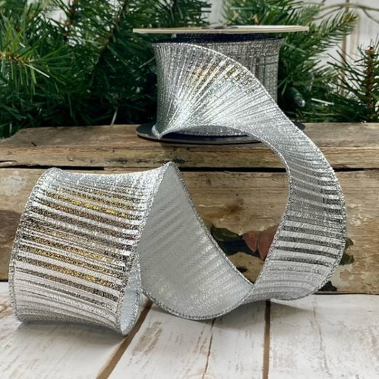 A silver fluted lame trim on a wooden surface with a blurred Christmas tree in the background.