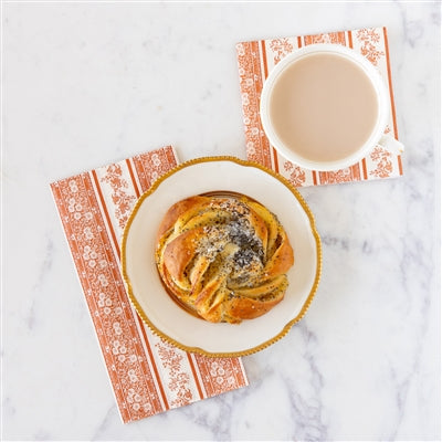 Baked pastry with a white bowl of cream on a decorative orange floral guest napkin over a marble surface