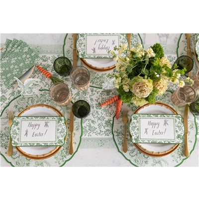 Easter table setting with place cards, carrots, and floral arrangements on a green patterned tablecloth.