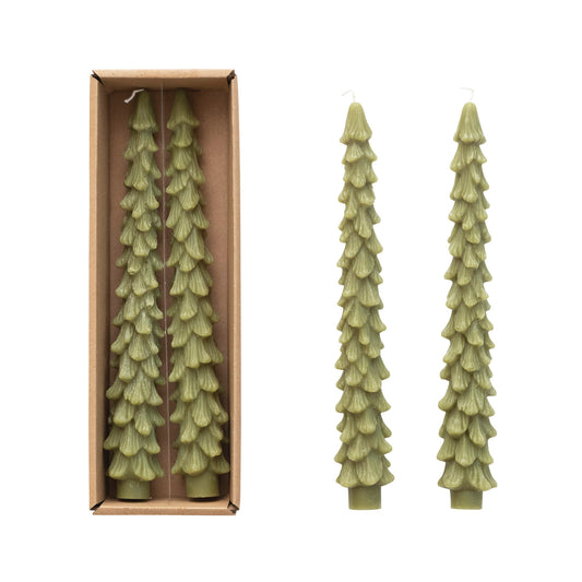 Two tall green candles shaped like evergreen trees next to a cardboard box containing more candles.