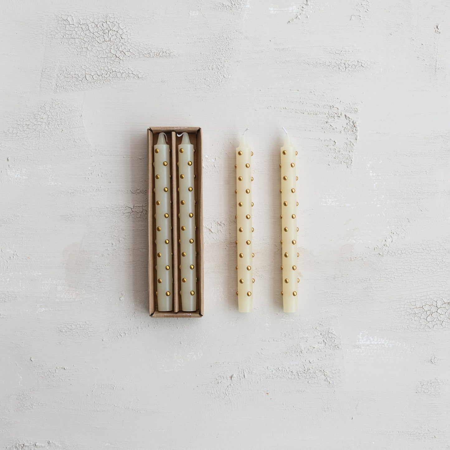 Set of two white candles with gold studs on a textured light gray surface