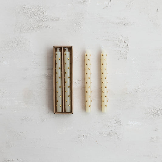 Set of two white candles with gold studs on a textured light gray surface
