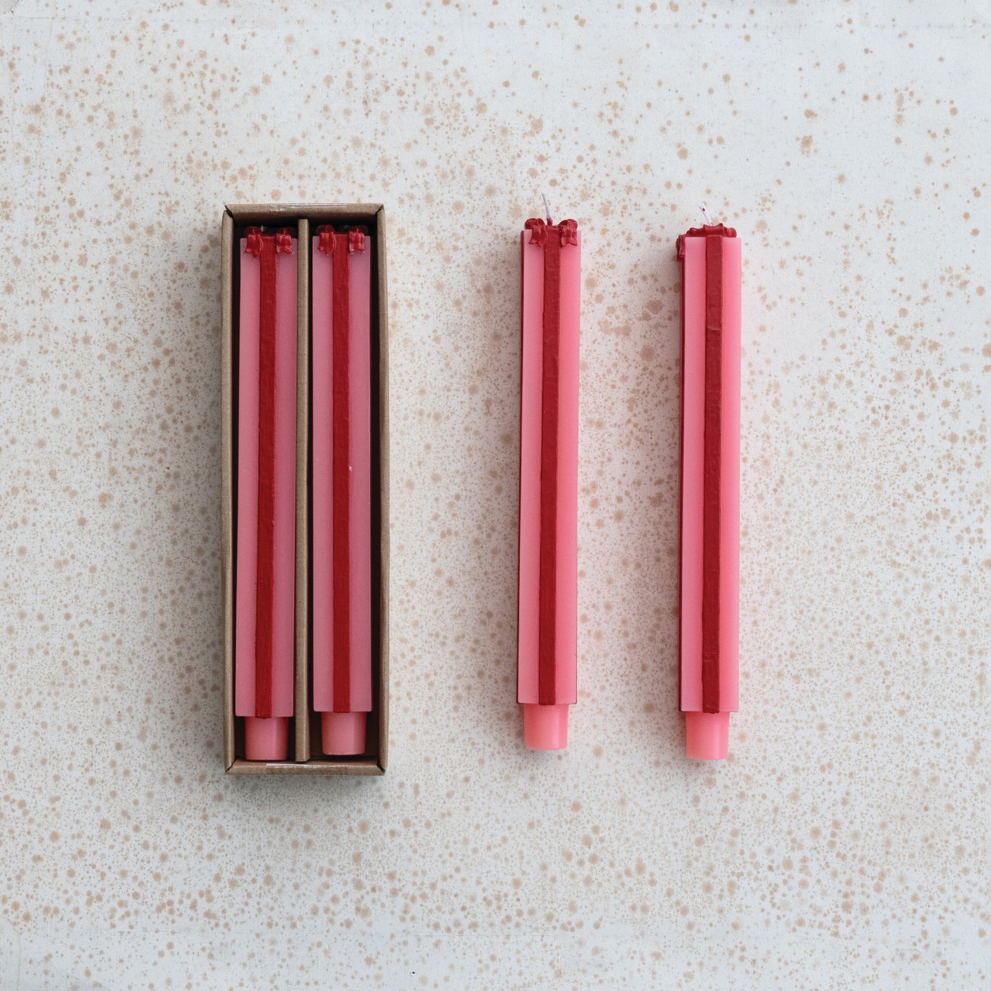 Set of red and pink candles shaped as gift boxes one candle outside its box on a speckled surface