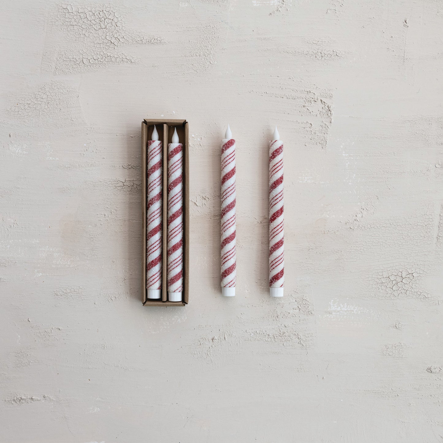 Set of striped LED candles with two candles outside its box on a light gray surface