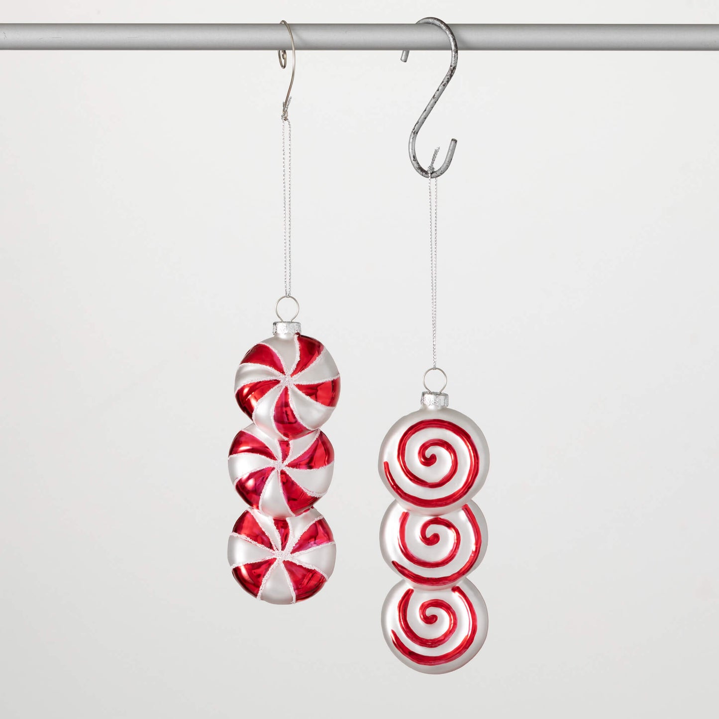 Two candy-shaped ornaments hanging from a metal hook; one is red and white striped like a candy cane, and the other is solid red.