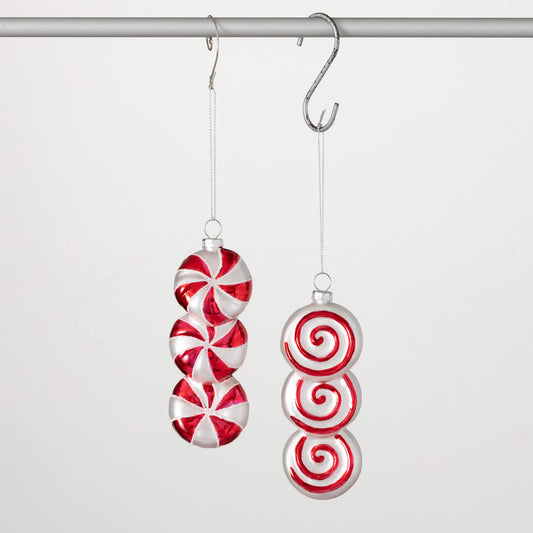 Two candy-shaped ornaments hanging from a metal hook; one is red and white striped like a candy cane, and the other is solid red.