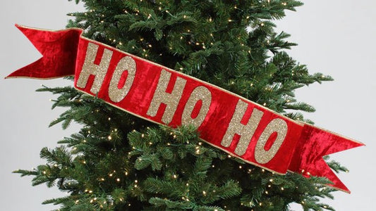 A red 'Ho Ho Ho' banner hanging on a Christmas tree.