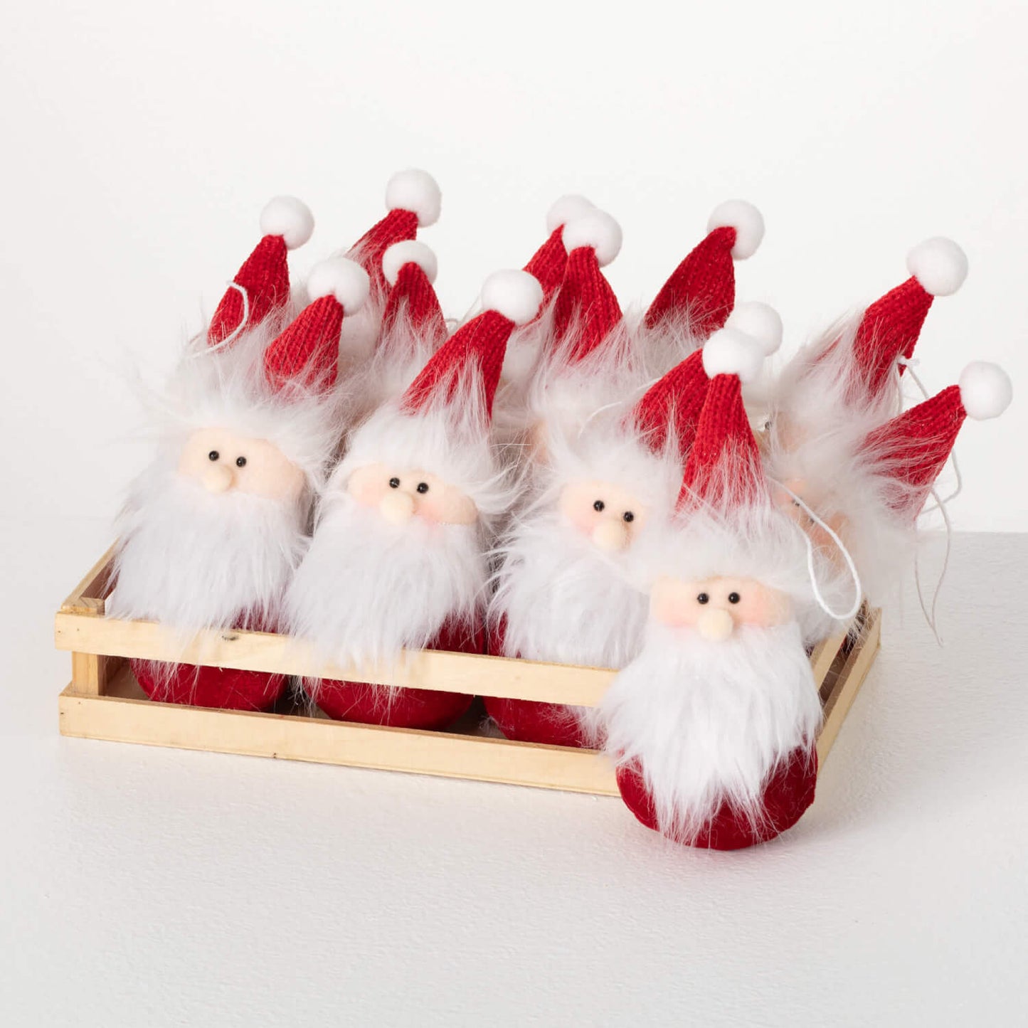A set of Santa Claus ornaments with red hats and white beards, placed in a wooden crate.