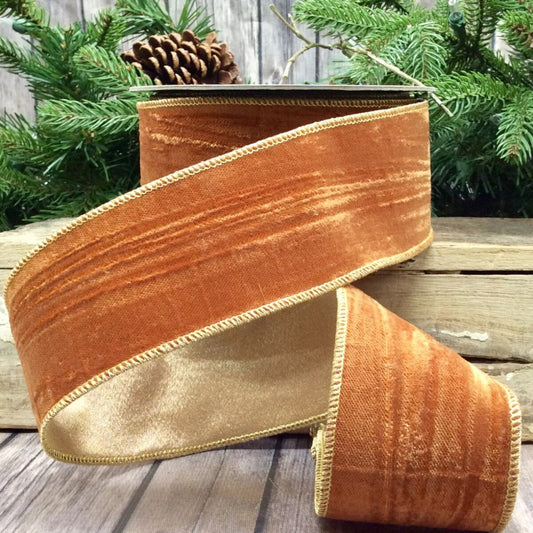 Orange and gold ribbon on a wooden surface with greenery in the background