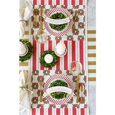 Decorative table setting with red and white striped tablecloth, green wreath centerpieces, and gold cutlery.