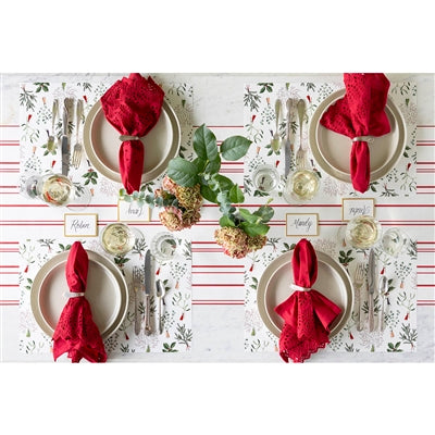 Christmas-themed table setting with red napkins, white plates, and a decorative tablecloth.