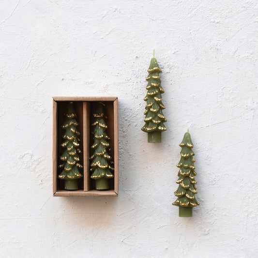 Green tree-shaped candles with gold accents on a textured white surface.