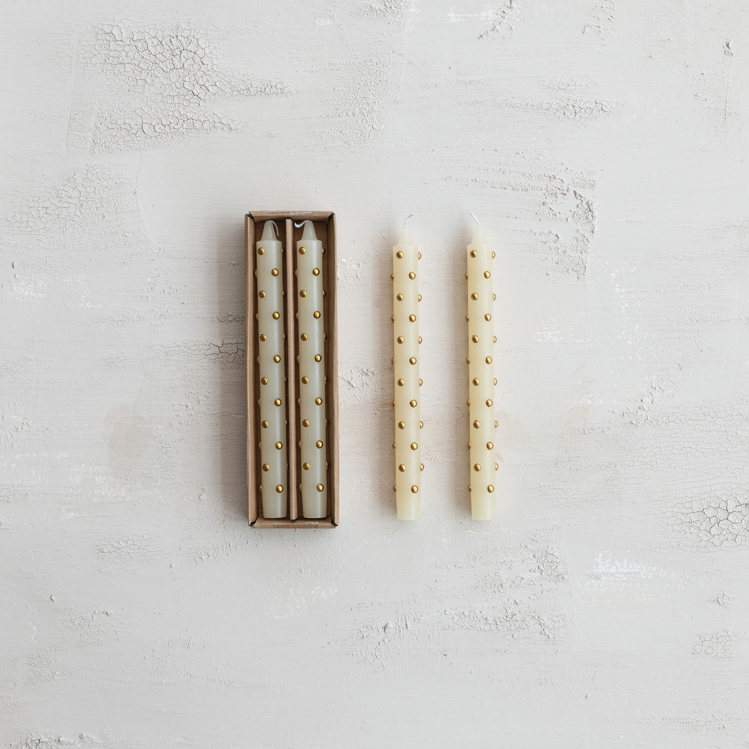 Set of two white candles with gold studs on a textured light gray surface