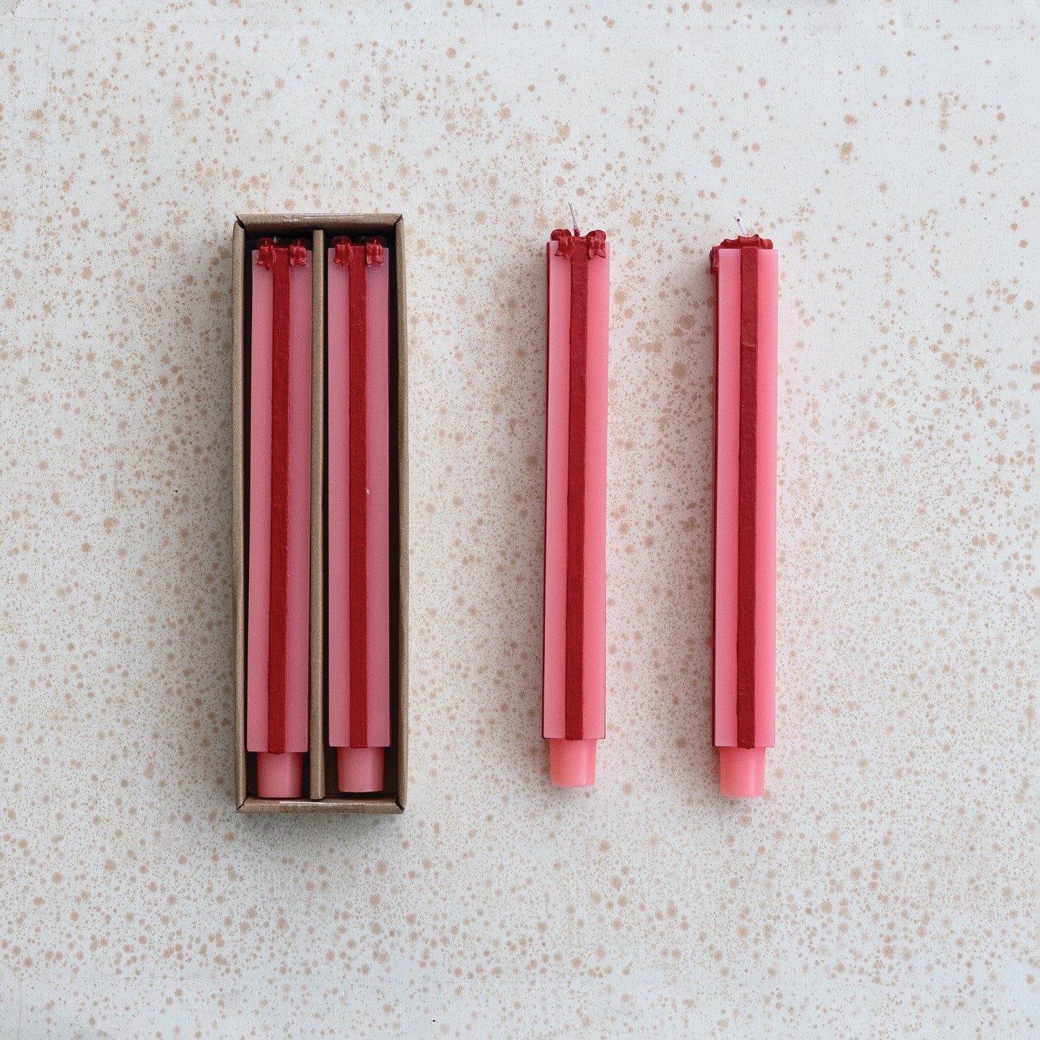 Set of red and pink candles shaped as gift boxes one candle outside its box on a speckled surface