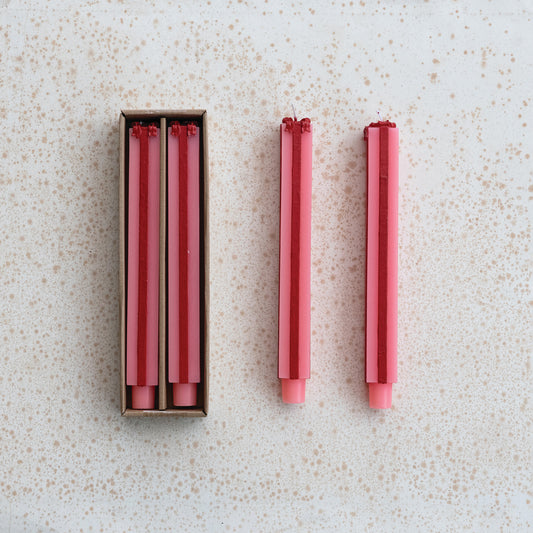 Set of red and pink candles shaped as gift boxes one candle outside its box on a speckled surface